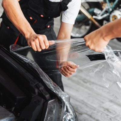 ppf-installation-process-close-up-stretching-removing-old-transparent-film-car-headlight-hood-by-hand-automobile-professional-service